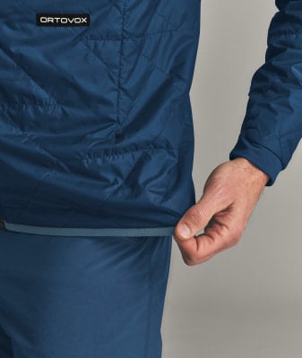 Detail einer Jacke mit ORTOVOX-Logo, Hand zieht Saum nach unten. Detail einer Jacke mit ORTOVOX-Logo, Hand zieht Saum nach unten.