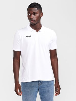 Ein Mann in einem weißen Poloshirt und Jeans vor neutralem Hintergrund.