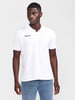 Ein Mann in einem weißen Poloshirt und Jeans vor neutralem Hintergrund.