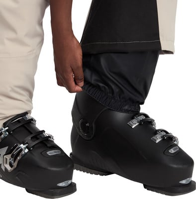 Eine Person passt eine schwarze Skihose über einen Skischuh an. Eine Person passt eine schwarze Skihose über einen Skischuh an.