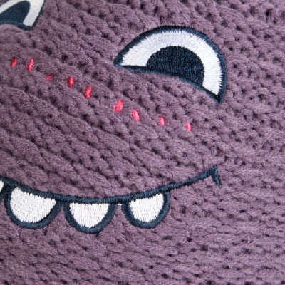 Detail einer Stickerei eines niedlichen lila Monsters mit großen Augen und einem Lächeln.