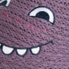 Detail einer Stickerei eines niedlichen lila Monsters mit großen Augen und einem Lächeln.
