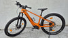 Ein orangefarbenes E-Bike mit schwarzen Rädern und Gabel steht auf dem Boden.