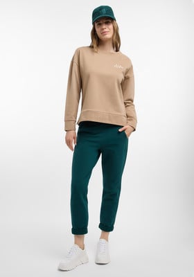 Frau in beigem Pullover, dunkelgrüner Hose und weißen Sneakern. Frau in beigem Pullover, dunkelgrüner Hose und weißen Sneakern.