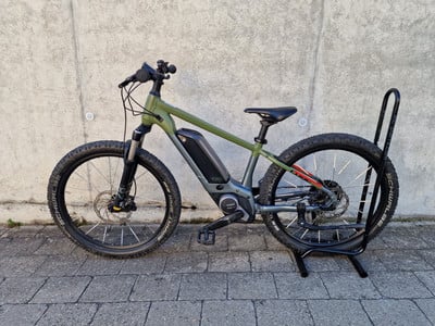 Grünes E-Bike mit schwarzem Ständer auf Kopfsteinpflaster vor einer Wand. Grünes E-Bike mit schwarzem Ständer auf Kopfsteinpflaster vor einer Wand.