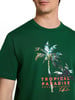 Zöld póló pálmafás mintával és Tropical Paradise felirattal.
