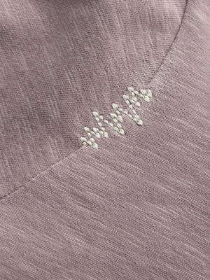 Detailaufnahme von hellviolettem Stoff mit weißer Stickerei.