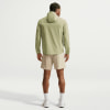 Ein Mann in einer grünen Kapuzenjacke und beige Shorts steht rückwärts.