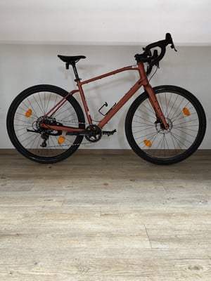 Ein rosafarbenes Gravelbike steht auf einem Holzboden vor einer weißen Wand.