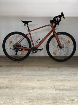 Ein rosafarbenes Gravelbike steht auf einem Holzboden vor einer weißen Wand.