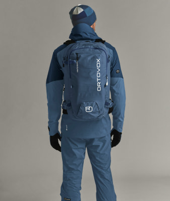 Mann von hinten in blauer Kleidung mit Ortovox-Rucksack.