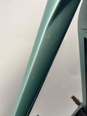 Detail eines Elektrofahrradrahmens mit leichten Kratzern auf der grünen lackierten Oberfläche.