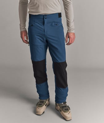 Ein Mann in blauer Skihose und beige Skischuhen steht vor grauem Hintergrund. Ein Mann in blauer Skihose und beige Skischuhen steht vor grauem Hintergrund.
