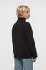 Ein Junge in einem dunklen Fleece-Pullover mit hohem Kragen und blauer Hose.