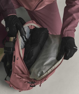Ein rosafarbener Rucksack mit einer schwarzen Jacke und Handschuhen darin.