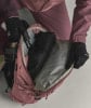 Ein rosafarbener Rucksack mit einer schwarzen Jacke und Handschuhen darin.