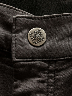 Detail eines Knopfes mit Logo auf dunkler Hose. Detail eines Knopfes mit Logo auf dunkler Hose.