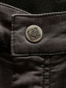 Detail eines Knopfes mit Logo auf dunkler Hose.
