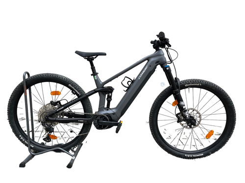 Graues Full-Suspension-E-Bike auf Ständer vor weißem Hintergrund.