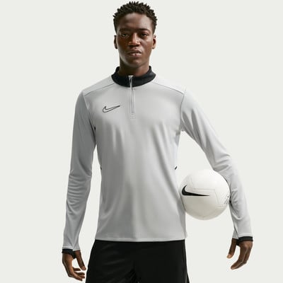 Ein Mann hält einen Fußball und trägt ein graues Langarmshirt.