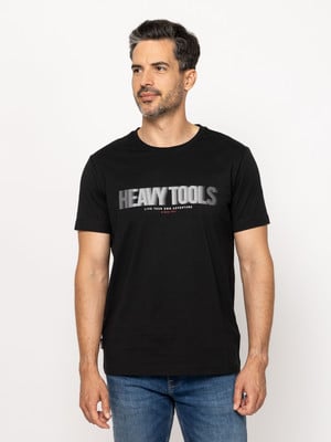 Egy férfi fekete pólóban, rajta HEAVY TOOLS felirat, kék farmerben. Egy férfi fekete pólóban, rajta HEAVY TOOLS felirat, kék farmerben.
