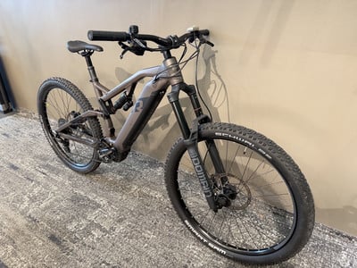 Ein graues E-Mountainbike mit Federung steht auf einem Teppich an der Wand. Ein graues E-Mountainbike mit Federung steht auf einem Teppich an der Wand.