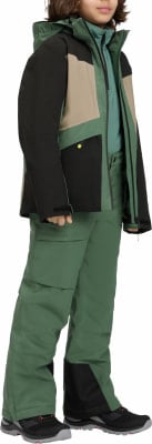 Junge in grüner Skijacke und Hose mit schwarzen und beigen Akzenten.
