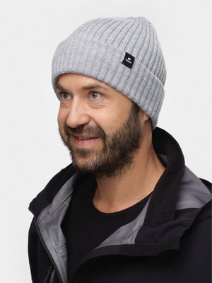 Ein Mann in einer grauen Strickmütze und schwarzer Jacke lächelt.