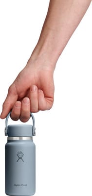 Eine Hand hält eine kleine blaue Hydro Flask Flasche am Henkel. Eine Hand hält eine kleine blaue Hydro Flask Flasche am Henkel.