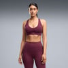 Eine Frau in weinroter Sportkleidung steht vor grauem Hintergrund.