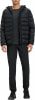 Ein Mann in einer schwarzen Daunenjacke mit Kapuze, schwarzer Hose und Schuhen.