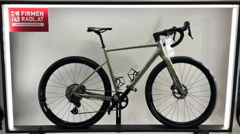 Ein helles Gravelbike mit schwarzen Rädern und Lenker steht auf einem Ständer.