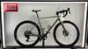Ein helles Gravelbike mit schwarzen Rädern und Lenker steht auf einem Ständer.