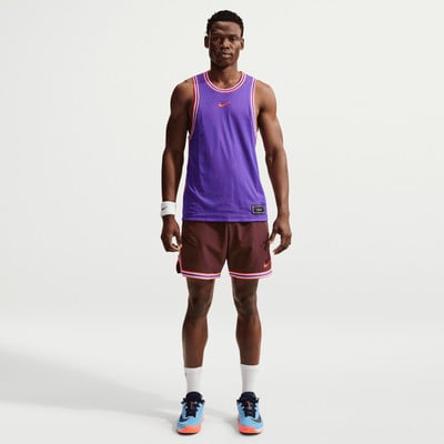 Ein Mann in einem lila Trikot und weinroten Shorts steht vor einem weißen Hintergrund.