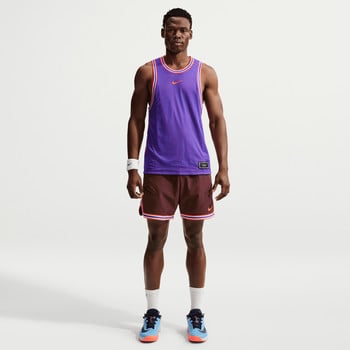 Ein Mann in einem lila Trikot und weinroten Shorts steht vor einem weißen Hintergrund.