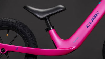 Ein pinkes Kinderfahrrad mit schwarzem Sattel und blauem Cube-Logo. Ein pinkes Kinderfahrrad mit schwarzem Sattel und blauem Cube-Logo.