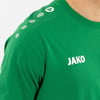 Grünes T-Shirt mit weißem JAKO-Logo und Details an den Schultern.