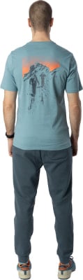 Mann von hinten in blaugrünem T-Shirt mit Bergmotiv und dunkler Hose. Mann von hinten in blaugrünem T-Shirt mit Bergmotiv und dunkler Hose.
