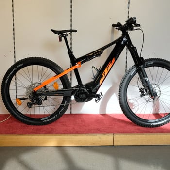 Schwarzes KTM E-Mountainbike mit orangefarbenen Akzenten auf rotem Teppich.