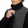 Ein Mann schließt eine schwarze Fleecejacke mit grauen Einsätzen und hohem Kragen.