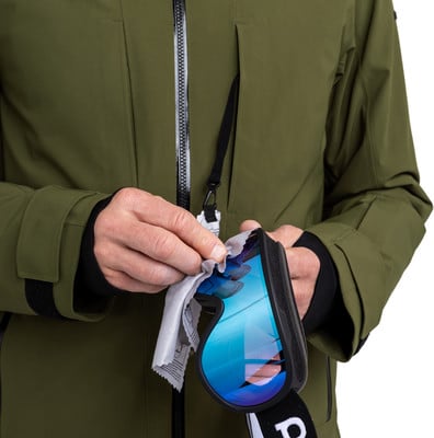 Ein Mann reinigt eine Skibrille mit einem grauen Tuch vor einer grünen Jacke. Ein Mann reinigt eine Skibrille mit einem grauen Tuch vor einer grünen Jacke.