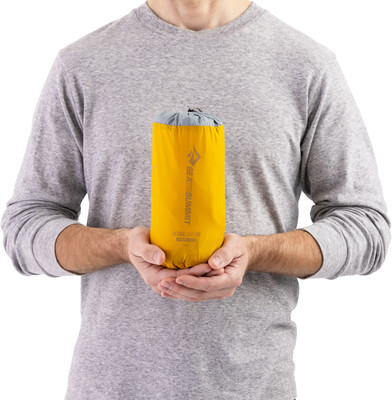 Ein Mann hält eine aufgerollte gelbe Tasche mit dem Logo von Sea to Summit in den Händen. Ein Mann hält eine aufgerollte gelbe Tasche mit dem Logo von Sea to Summit in den Händen.
