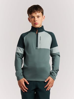 Junge in dunkelgrünem Pullover mit halbem Reißverschluss und Farbblöcken.