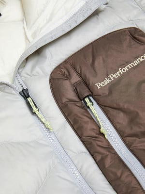 Detail einer Jacke mit Peak Performance Logo und Reißverschlüssen in Weiß und Braun. Detail einer Jacke mit Peak Performance Logo und Reißverschlüssen in Weiß und Braun.