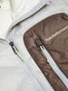 Detail einer Jacke mit Peak Performance Logo und Reißverschlüssen in Weiß und Braun.