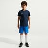 Junge in dunkelblauem Nike-T-Shirt und blauen Shorts mit weißen Socken.