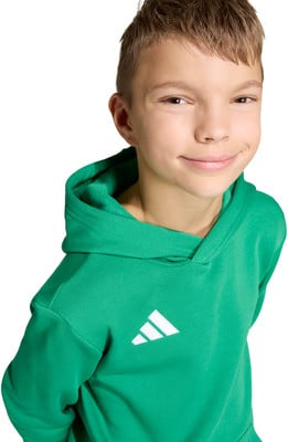 Ein Junge in einem grünen Hoodie mit Adidas-Logo lächelt vor weißem Hintergrund.