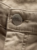 Detail eines Knopfes mit Markenlogo auf einer beigen Hose.