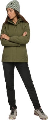 Eine Frau in einer grünen Jacke, schwarzen Hose und gestreifter Mütze steht mit verschränkten Armen. Eine Frau in einer grünen Jacke, schwarzen Hose und gestreifter Mütze steht mit verschränkten Armen.