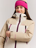 Junges Mädchen in einer beigen Jacke und pinker Mütze vor grauem Hintergrund.